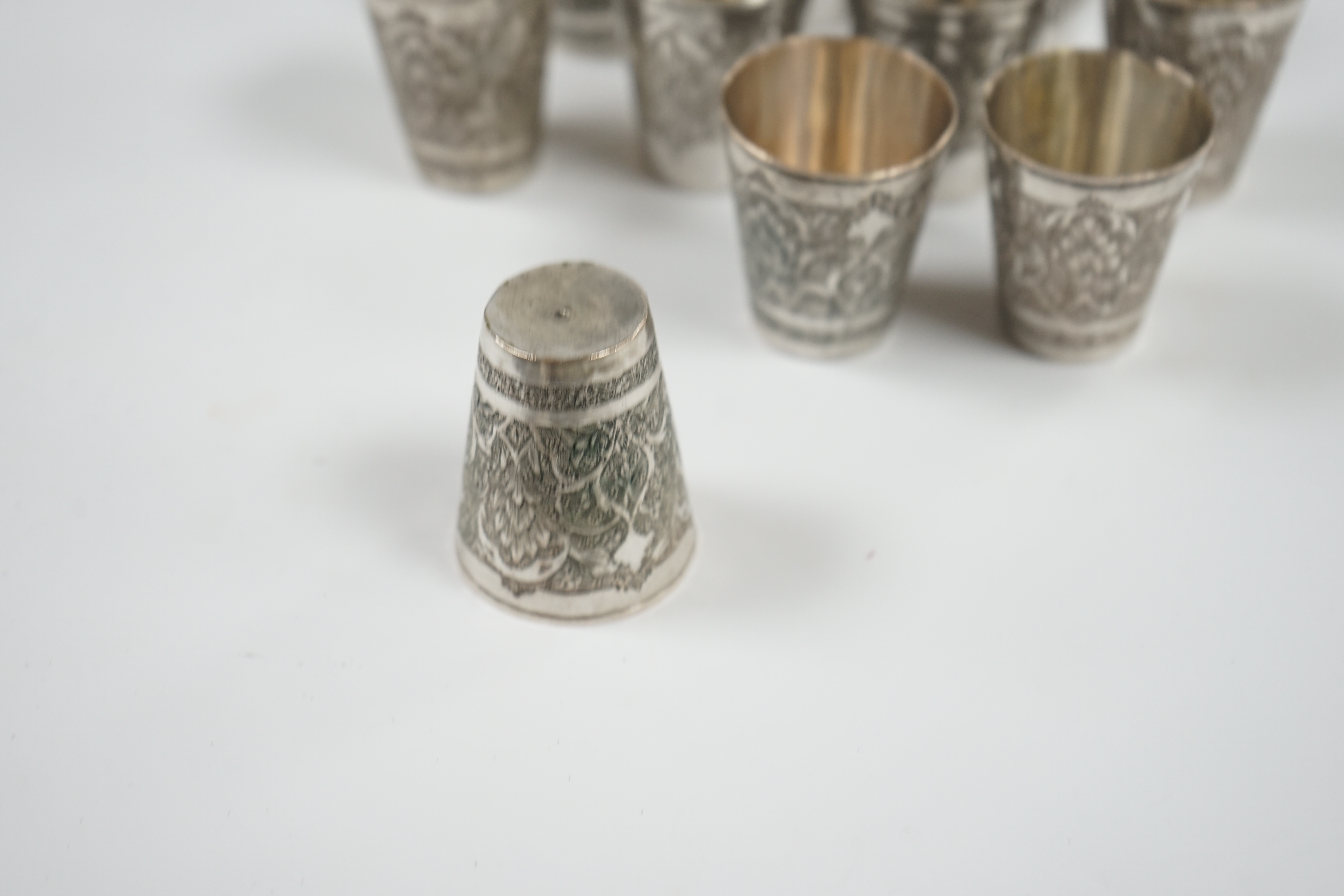 A set of four Persian engraved white metal tot cups, 43mm, stamped marks to the base and six other similar tot cups, 44mm, 8.7oz. Condition - fair